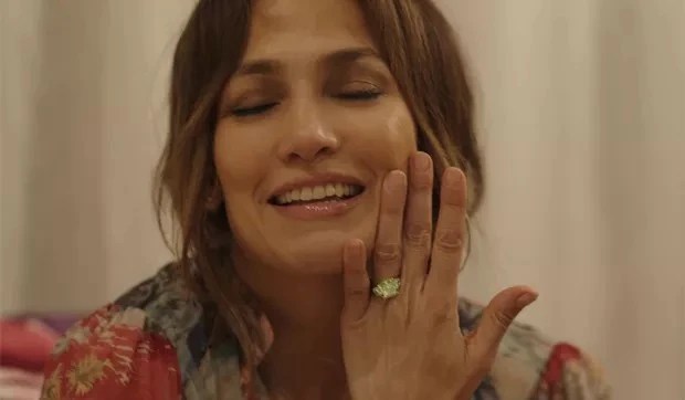 Jennifer Lopez, uma mulher morena e de cabelos castanhos, exibe em sua mão um anel de noivado de diamante verde