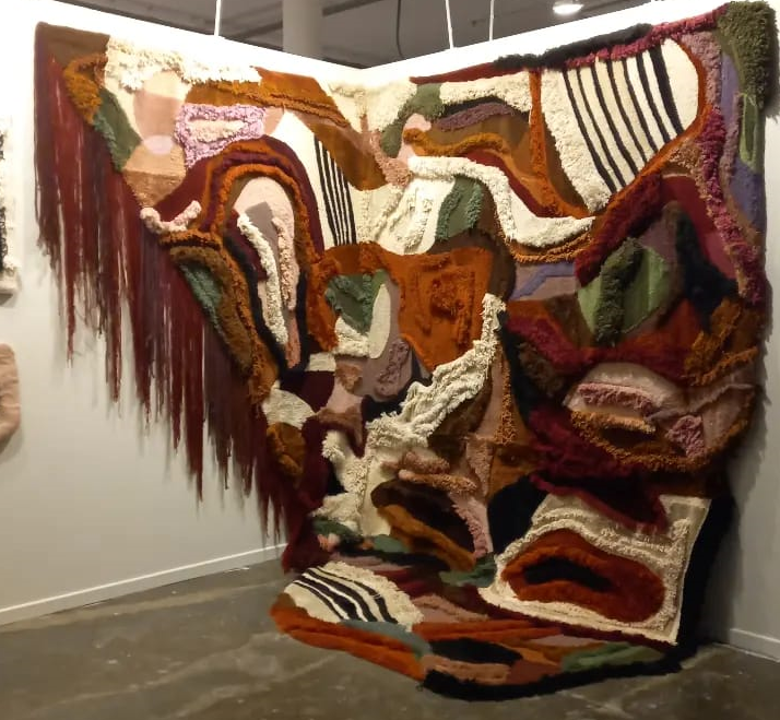 Tapeçaria colorida de Alex Rocca que toma uma duas das paredes e o chão de um estande
