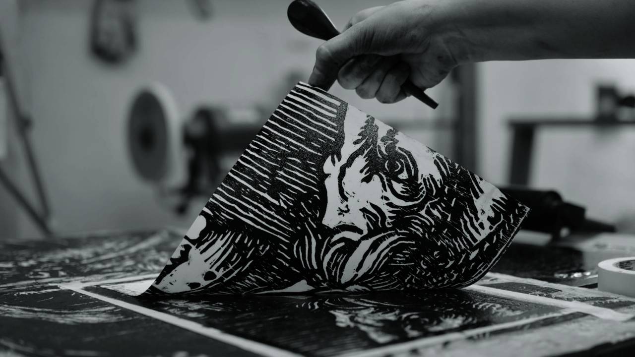 Imagem em preto e branco mostra pessoa retirando papel com impressão de mesa com tinta