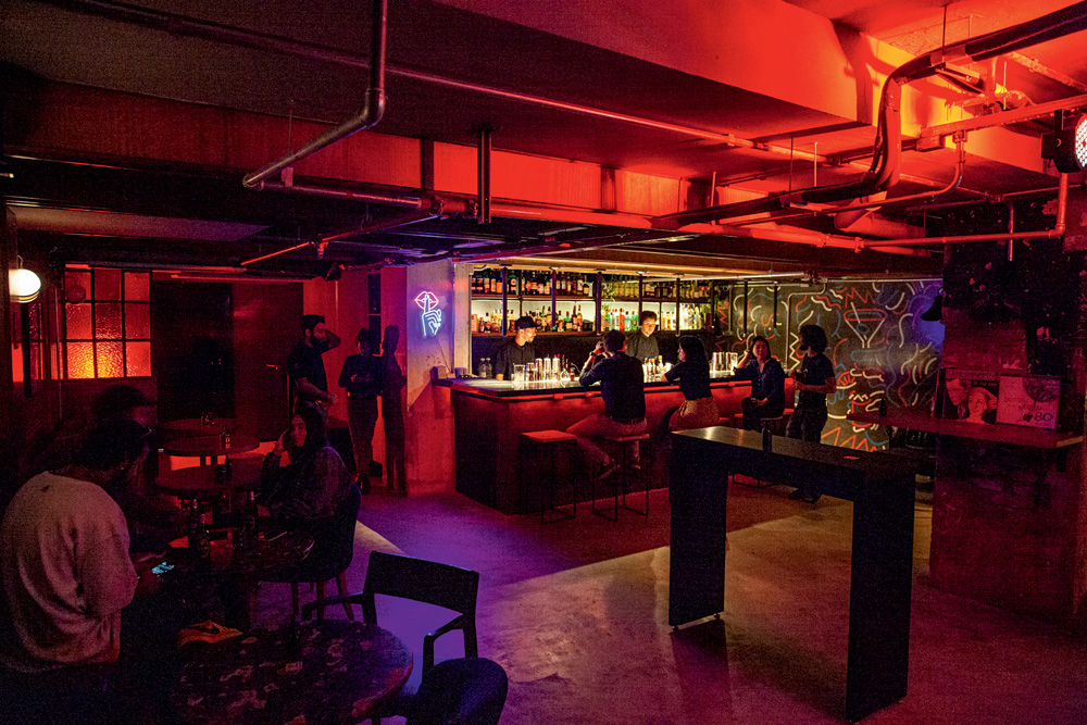Ambiente de um bar com balcões, mesas e cadeiras, iluminados por uma luz vermelha fraca