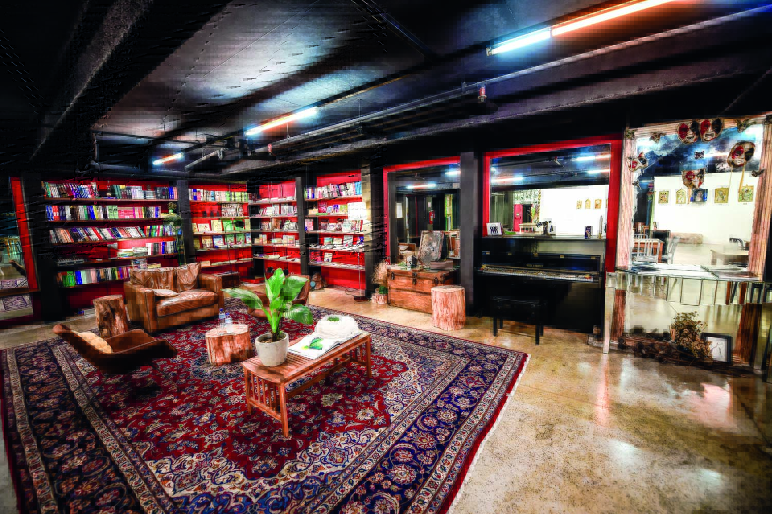 Imagem mostra interior de espaço com tapete estampado, colorido, e estantes com livros ao fundo