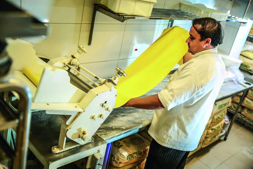 Imagem mostra cozinheiro colocando massa em aparelho culinário