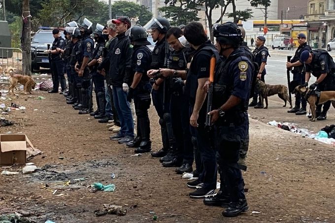 Fileira de policiais em parque com chão de barro.