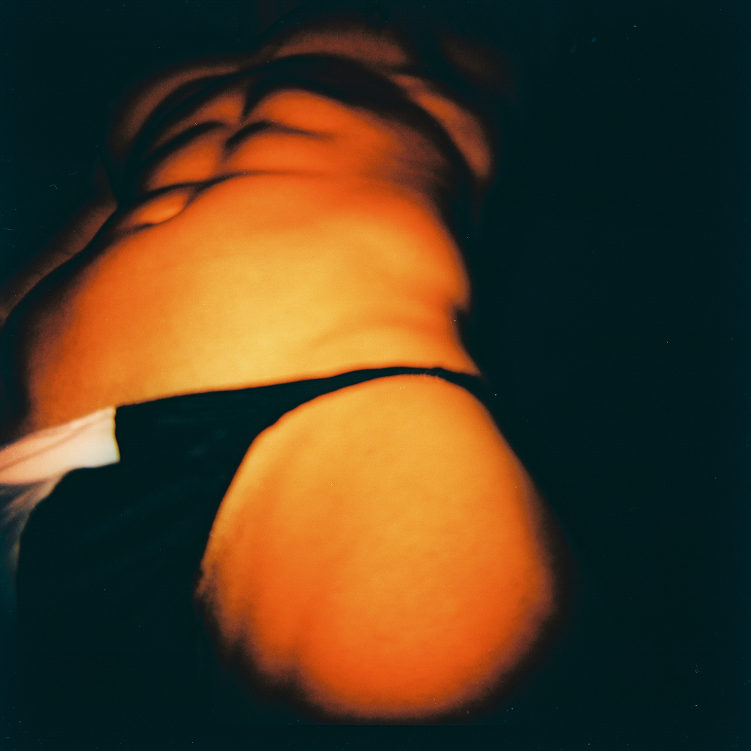 Imagem exibe, de baixo, um torso musculoso vestindo uma tanga preta. A foto tem tons amarelados.
