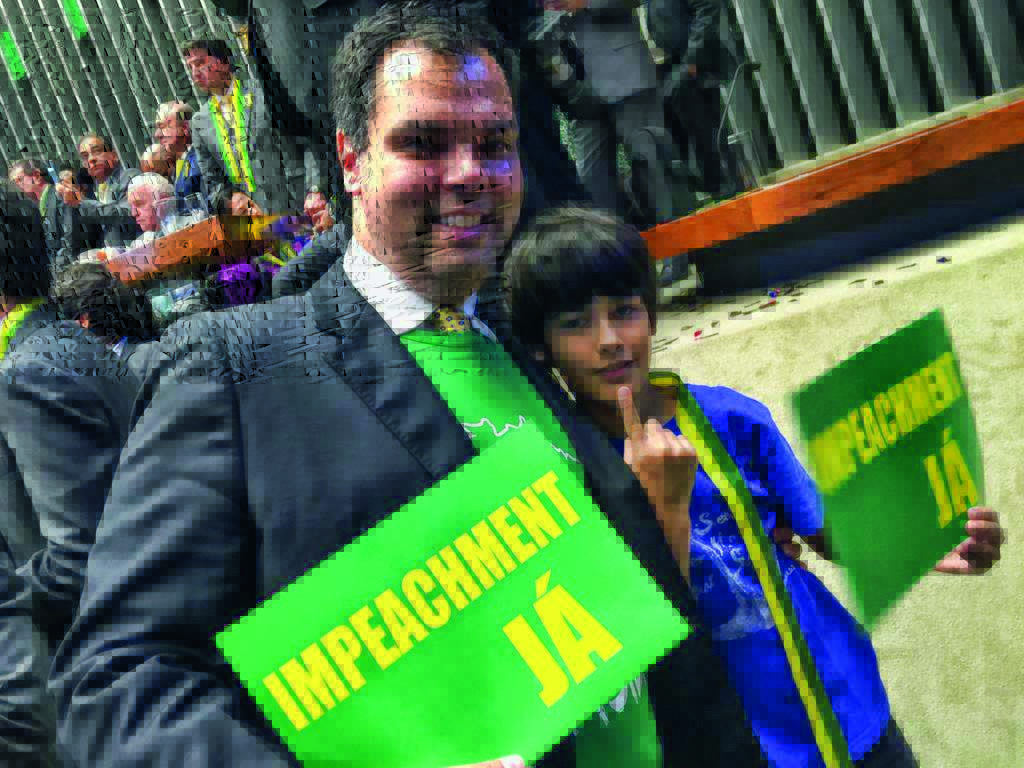 Bruno Covas, de terno, ao lado do seu filho, Tomás. Eles seguram placas verdes onde está escrito 