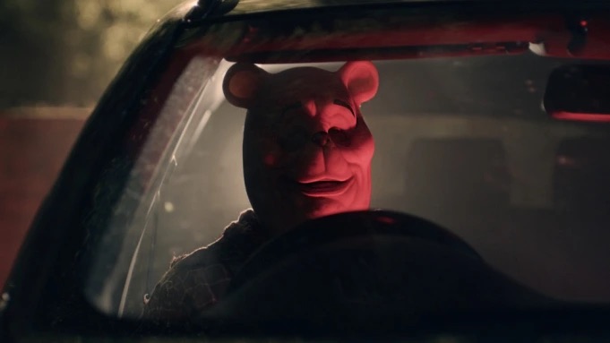 Imagem mostra pessoa com máscara de urso dentro de carro, iluminada por luz vermelha