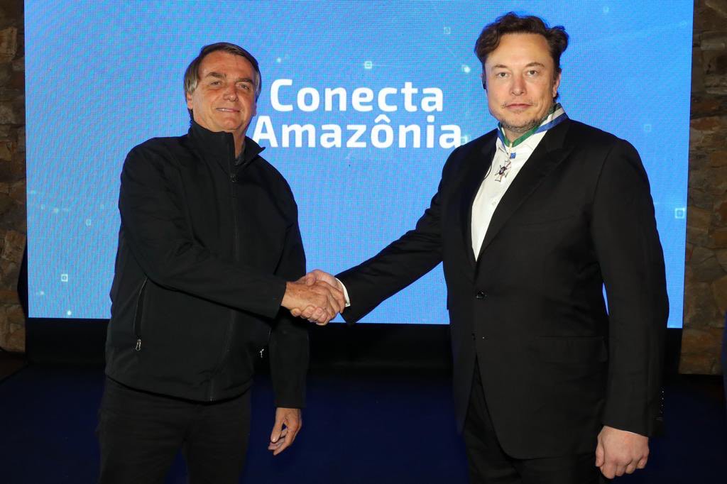 Imagem mostra dois homens apertando as mãos. Ao fundo, um telão azul escrito "Conecta Amazônia".