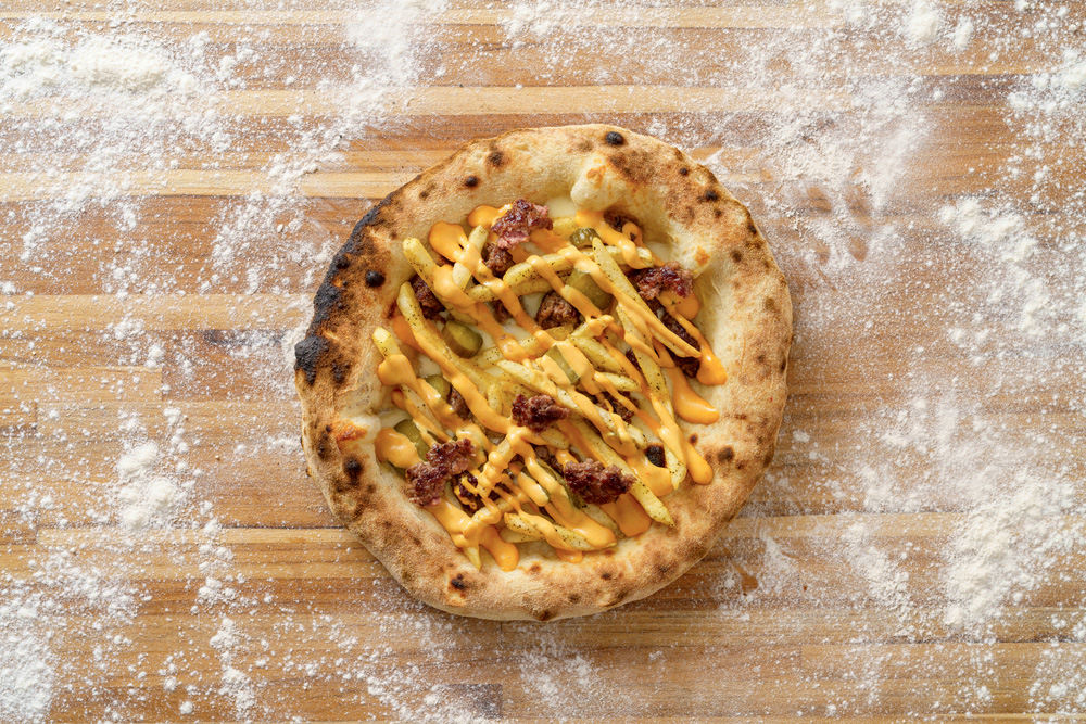 Pizza vista de cima com fios de queijo amarelado e pedaços de carne