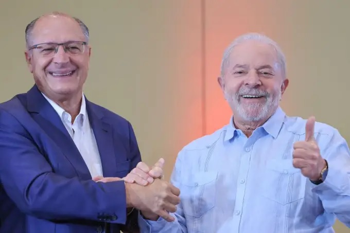 Alckmin e Lula Posam com as mãos dadas, sorrindo.
