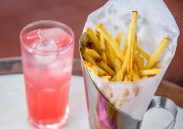 Imagem mostra um copo com um líquido rosa e uma porção de batatas fritas.