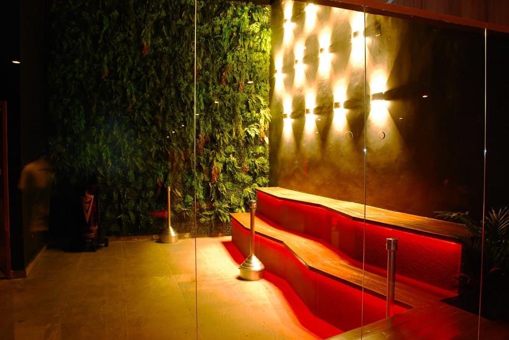 Ambiente da Pamaris Eventos tem parede de espelhos, outra repleta de plantas e sofá vermelho.