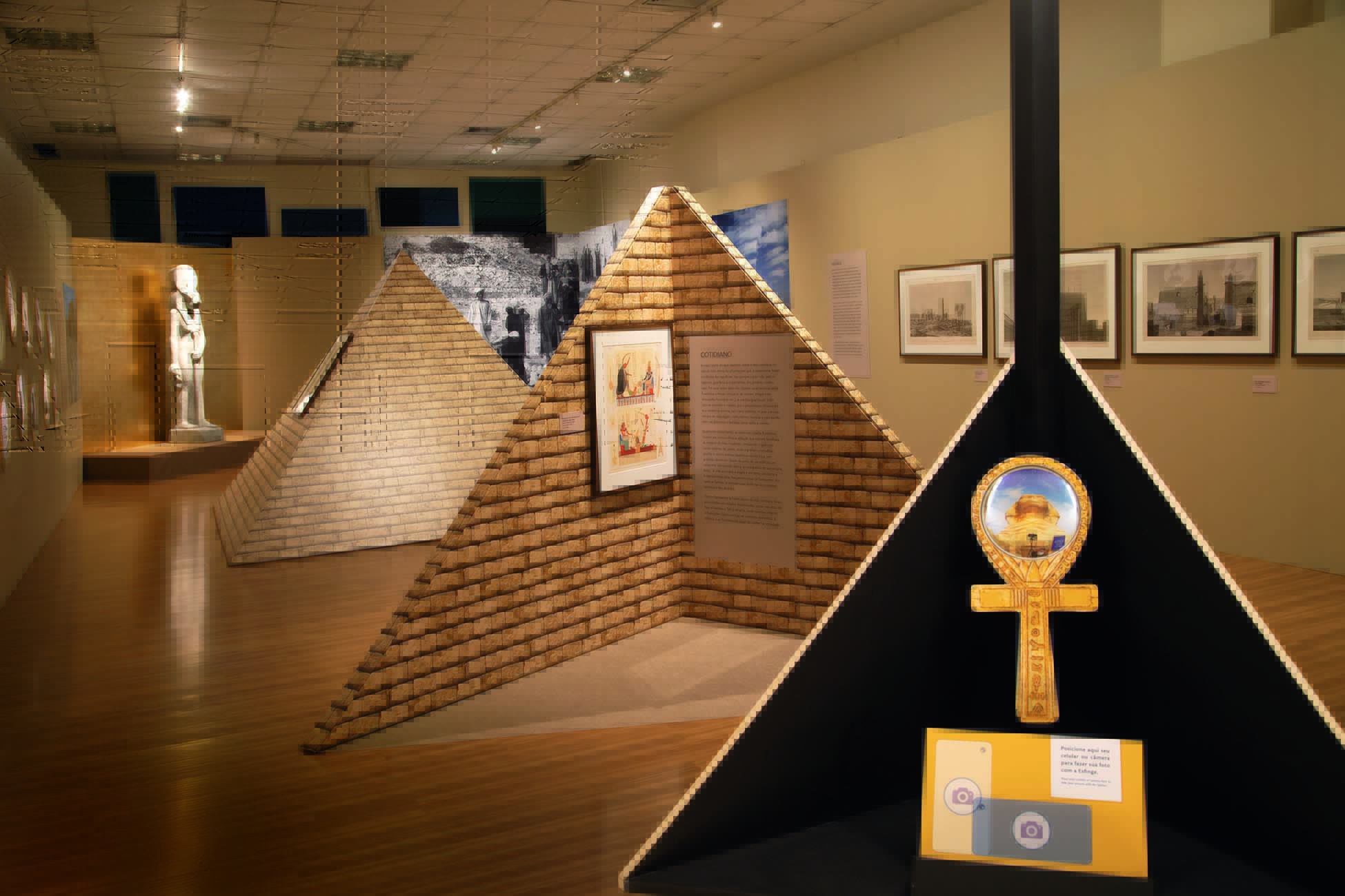 Imagem mostra sala iluminada com representações de pirâmides ao centro.