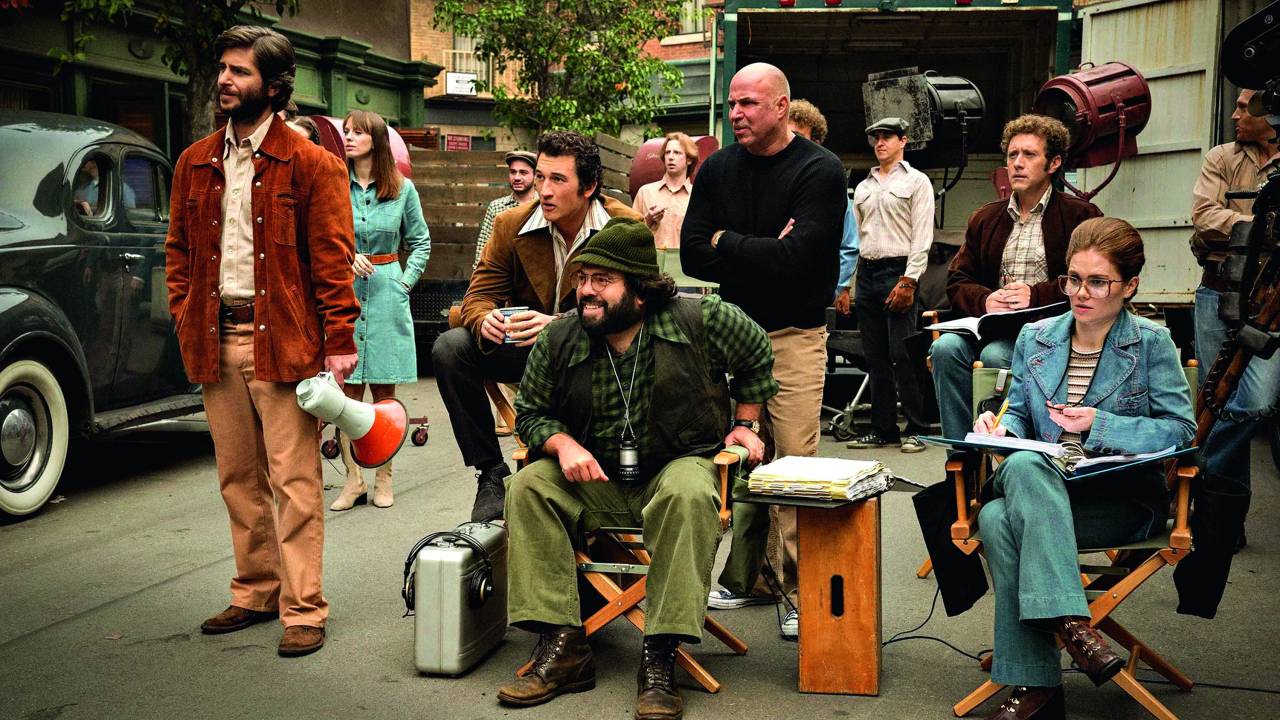 Imagem mostra diversas pessoas em set de filmagem, olhando para a esquerda. Ao centro, um homem barbudo, o diretor, sentado em uma cadeira.