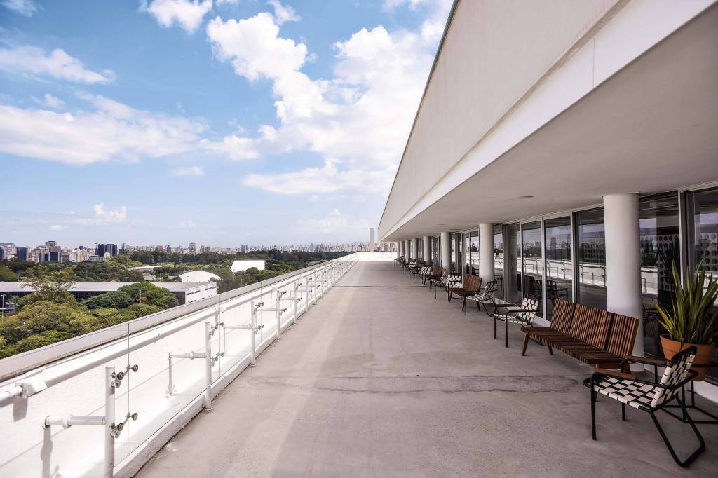 Foto mostra sacada do MAC, onde fica o restaurante Vista. O céu está azul, com poucas nuvens. Cadeiras e mesas em tons terrosos estão no canto direito