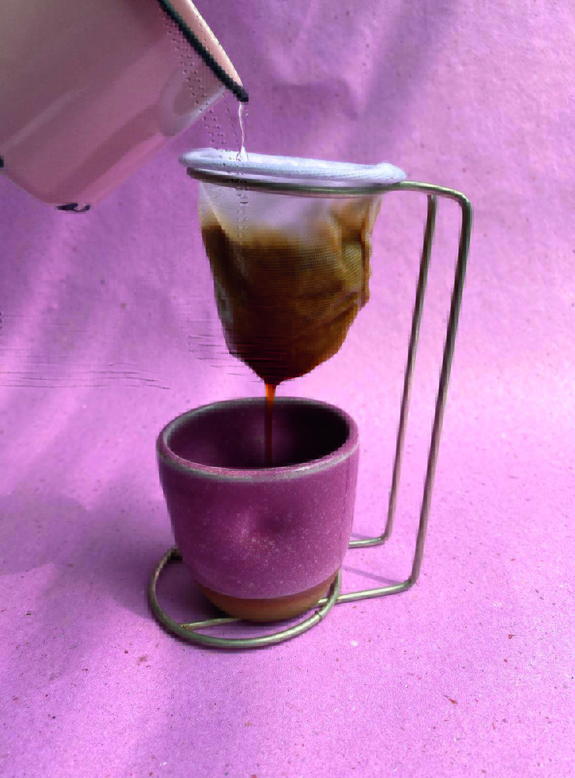 Foto de uma xícara de café de cerâmica rosa embaixo de um coador na frente de uma parede de cor rosa