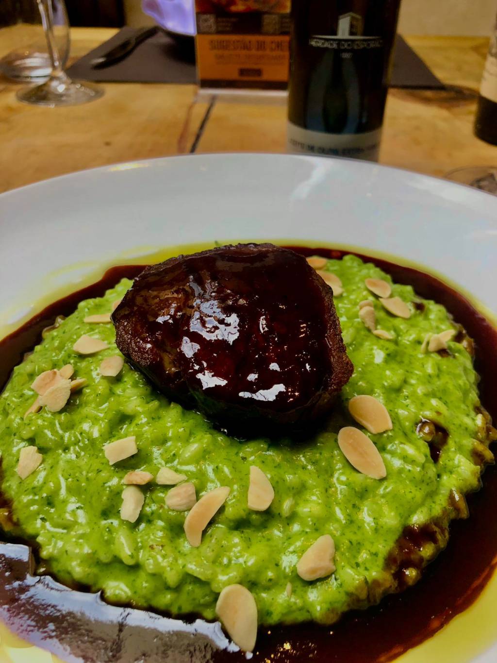 Risoto de cor esverdeada salpicado com lascas de amêndoas e., sobre ele, um medalhão de fié-mignon