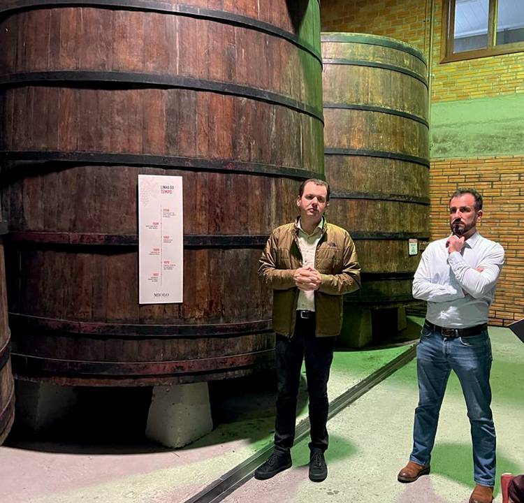 Adriano Miolo e Miguel Almeida posam em frente a barris de vinho