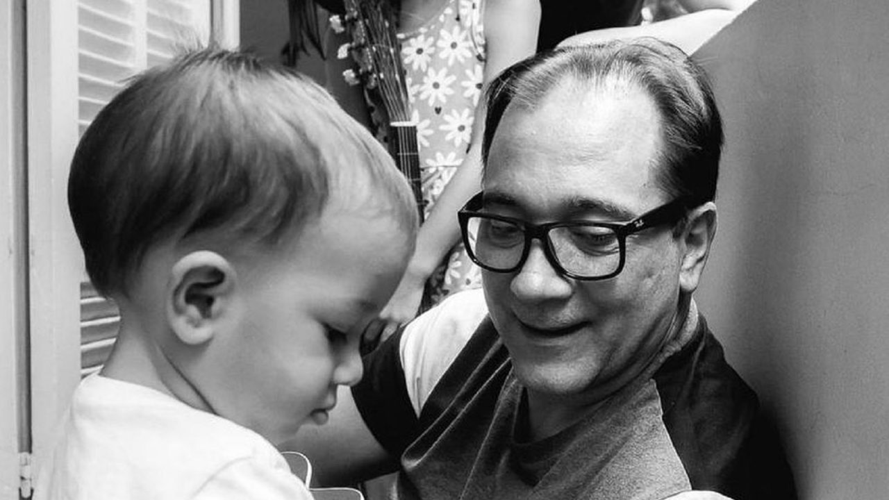 Bruno Gouveia ao lado do filho bebê em foto preto e branco.