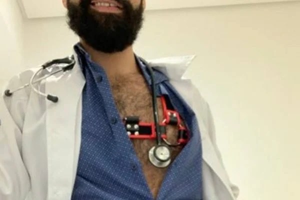 Imaem mostra homem com camisa aberta mostrando estetoscópio sobre o peito.