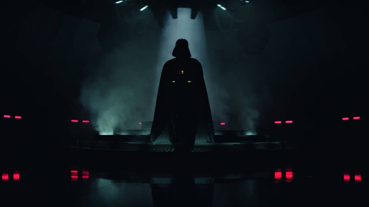 Imagem escura mostra silhueta do vilão Darth Vader em ambiente com luzes vermelhas no chão
