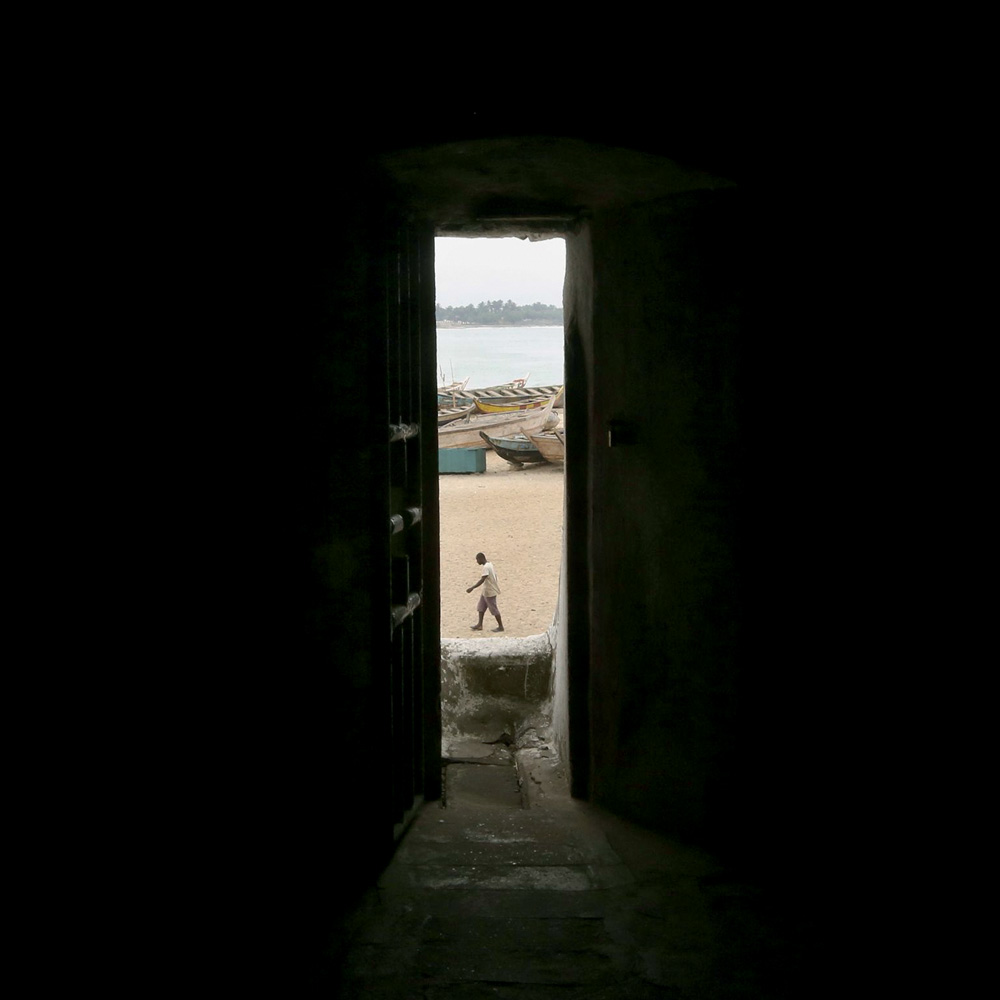 1. Gana, Porta do não-retorno.jpg Imagem mostra fresta de porta mostrando praia com um homem caminhando na areia