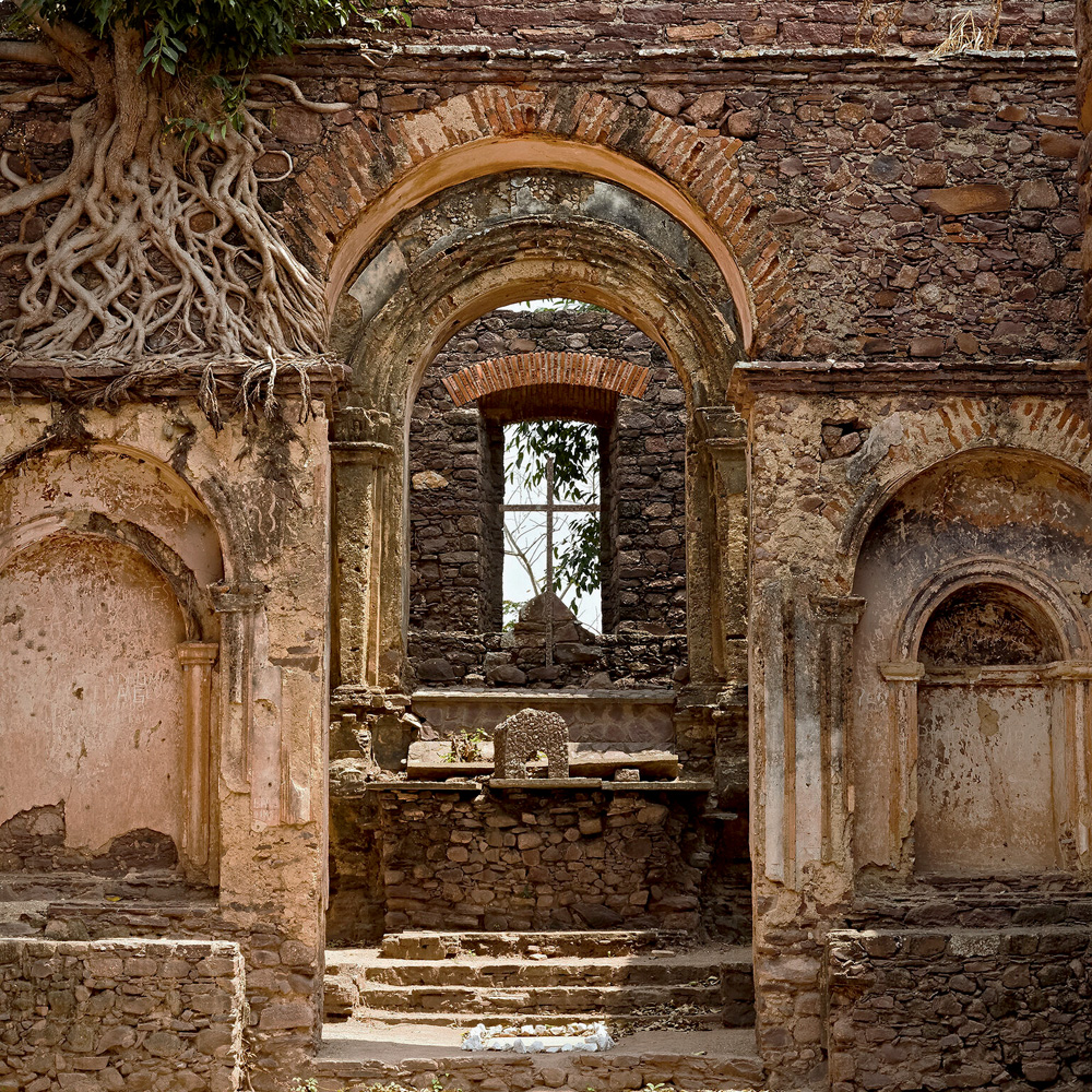 Imagem mostra construção antiga com raízes de árvores tomando as paredes de pedra.