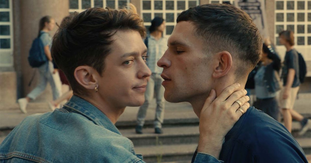 Imagem mostra dois homens, um de olhos fechados, pronto para beijar o outro, que está olhando para o lado