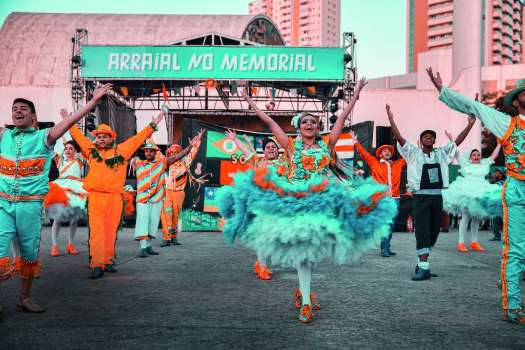 Imagem mostra pessoas com roupas festivas das cores azul e laranja, dançando em espaço aberto