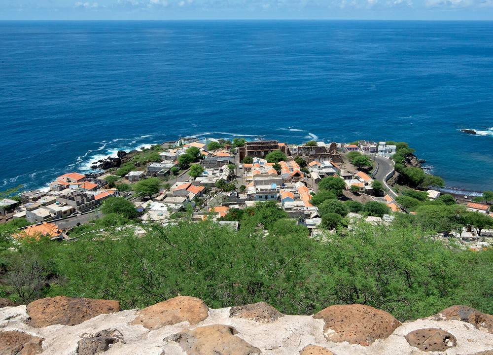 Imagem mostra pedaço de terra com casas e vegetação envolto por um horizonte de mar.