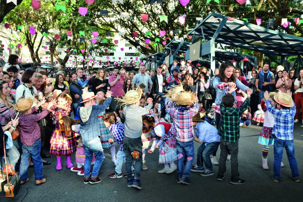 Imagem mostra crianças com roupas de festa junina em pátio aberto