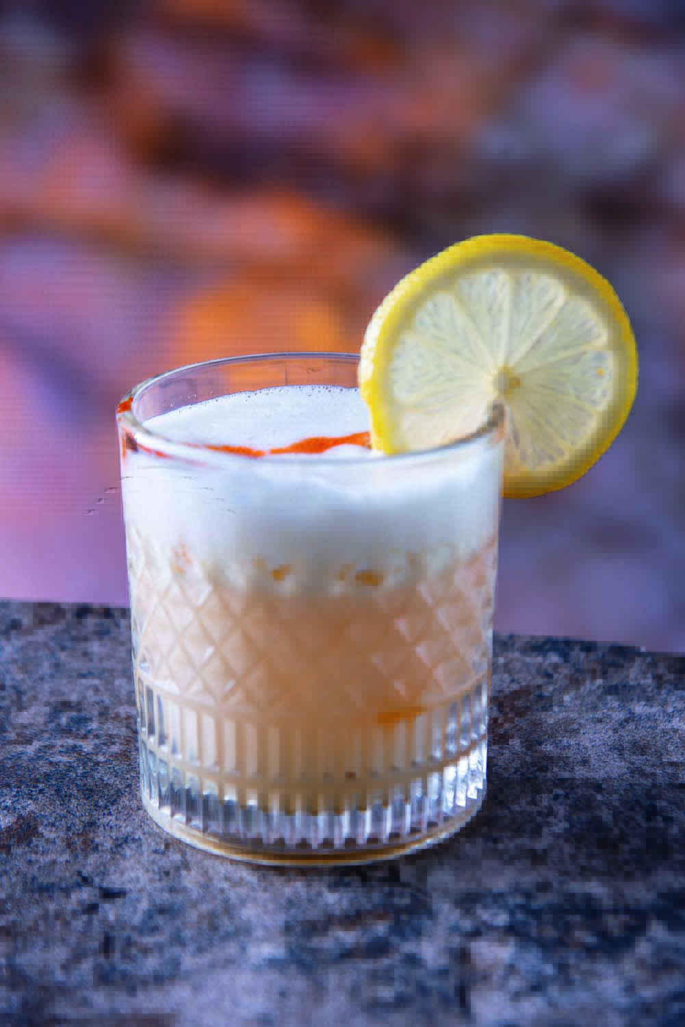Drinque de cor clara servido em copo redondo e baixo e decorado por uma rodela de limão siciliano