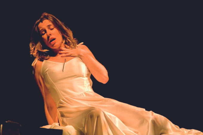 Imagem mostra mulher de vestido branco com a mão sobre o pescoço, inclinada