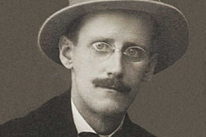 James Joyce em retrato em preto e branco. Ele é um homem de meia-idade, branco e magro. Usa chapéu, óculos e bigode. Também veste um terno preto com gravata borboleta