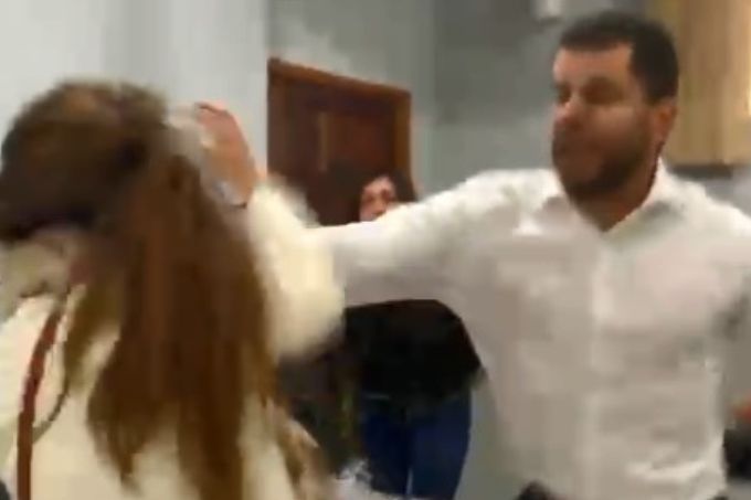Um homem branco agredindo uma mulher branca de cabelos longos dentro de um escritório