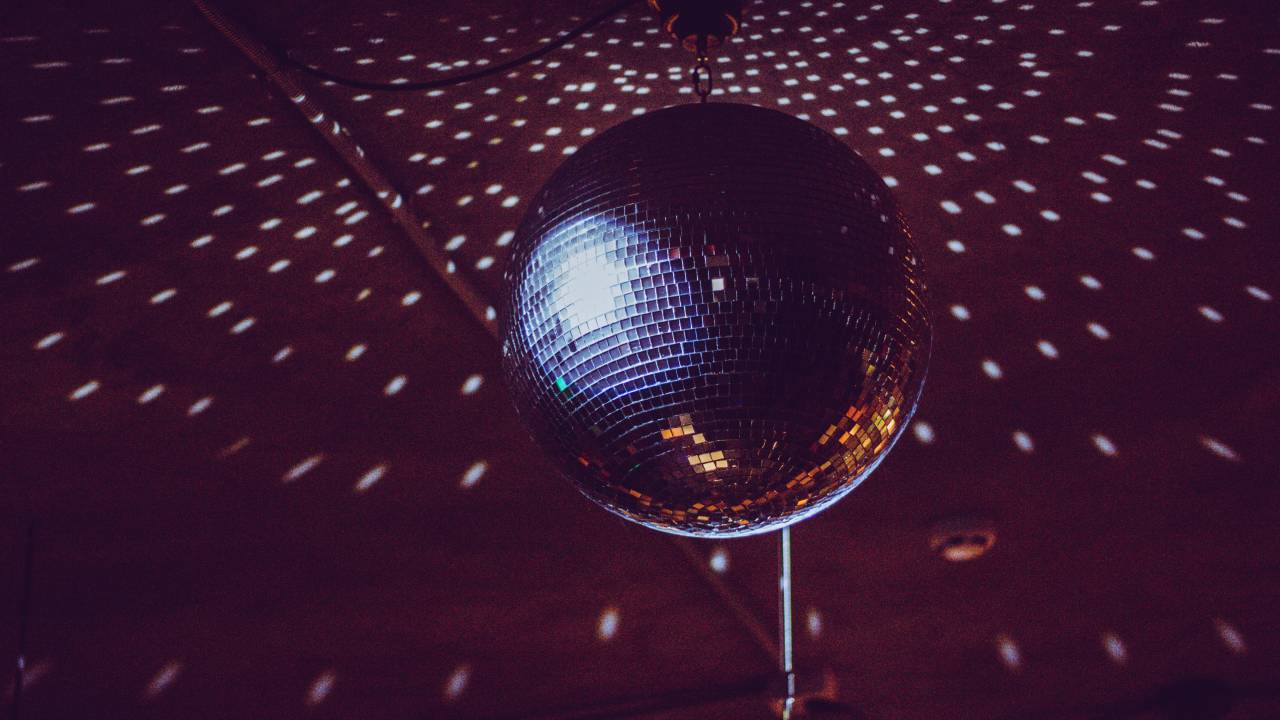 Foto exibe bola iluminada de discoteca com pontinhos brancos espalhados pelo teto.