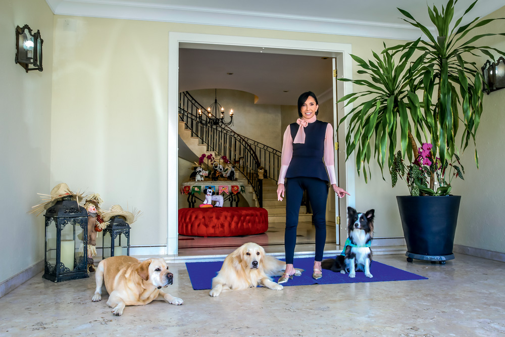 Iara Souto, do Pet Palazzo, posa de pé em frente a mansão com três cachorros ao redor.