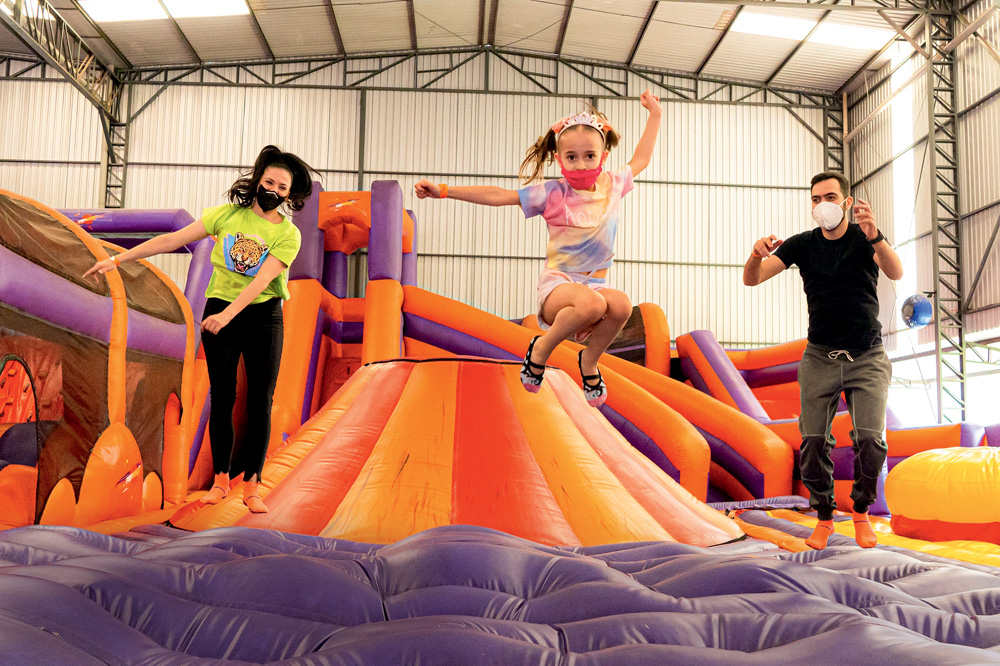 Duas meninas e um adulto pulam em um brinquedo inflável colorido