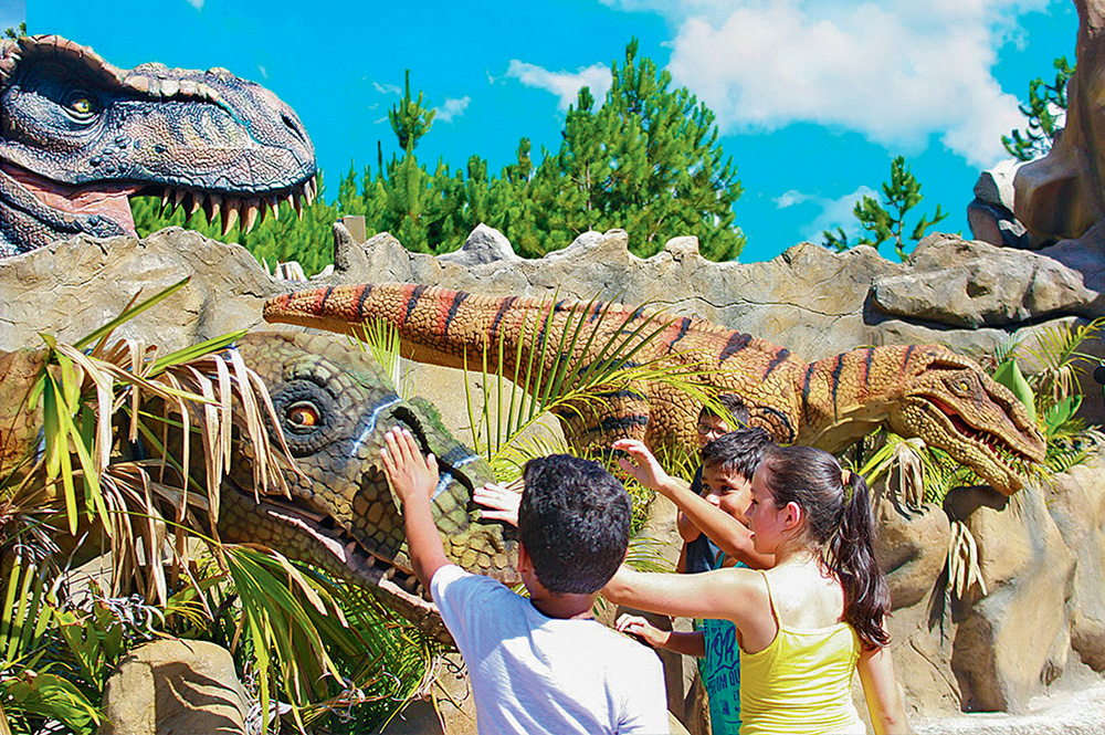 Três crianças tocam em uma réplica de dinossauro