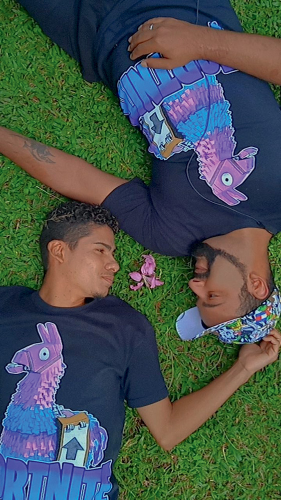 Carlos e Raphael estão deitados na grama, em lados opostos e sorriem levemente