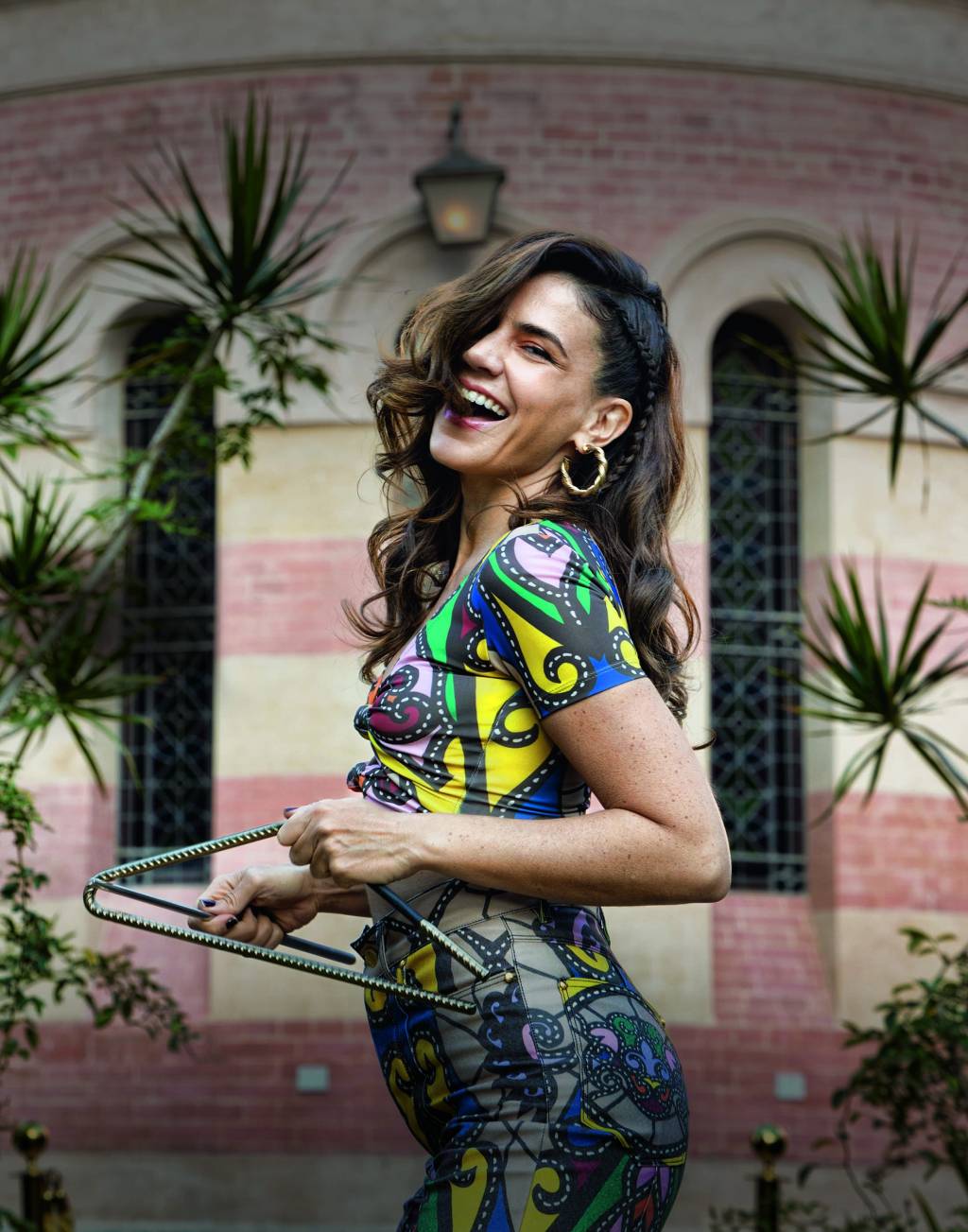 Imagem mostra mulher de roupa colorida, sorrindo e tocando triângulo.