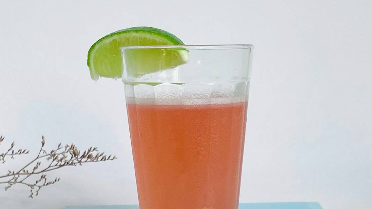 Drinque de cor rosa clara é servido em copo americano decorado por uma fatia de limão