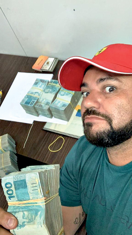 Imagem mostra maços de dinheiro sobre uma mesa e homem de boné vermelho em primeiro plano