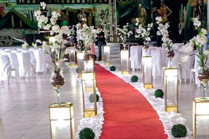 Decoração do casamento comunitário celebrado no Dia dos Namorados: tapete vermelho, arranjos de flores brancos, pequenos arbustos no chão
