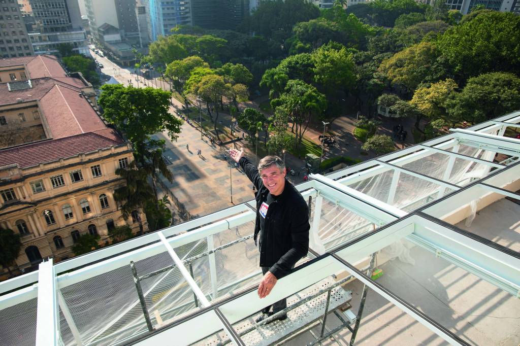 Olivier no anexo do Rooftop. Um homem de meia-idade e branco com um dos braços estendidos, mostrando a vista abaixo