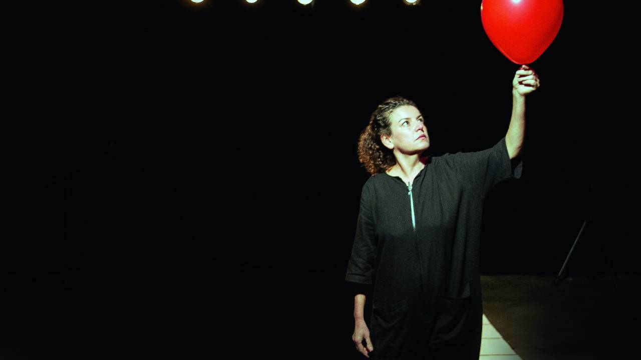 Eloisa Elena segura um balão vermelho em um palco de cenário monocromático preto