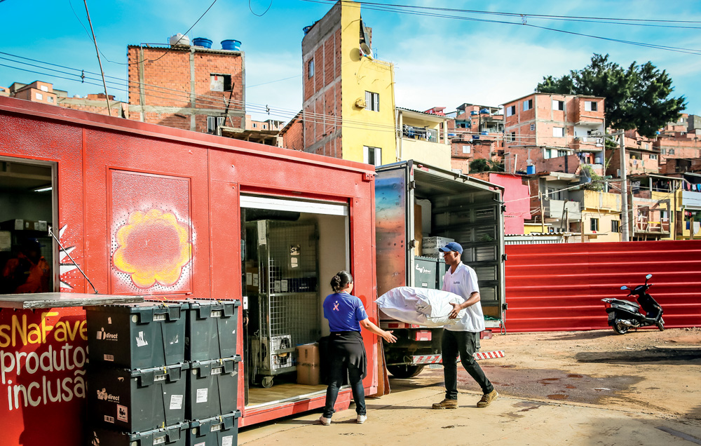 Dois trabalhadores, um homem e uma mulher, descarregam um caminhão e um contêiner com pacotes e caixas, em Paraisópolis