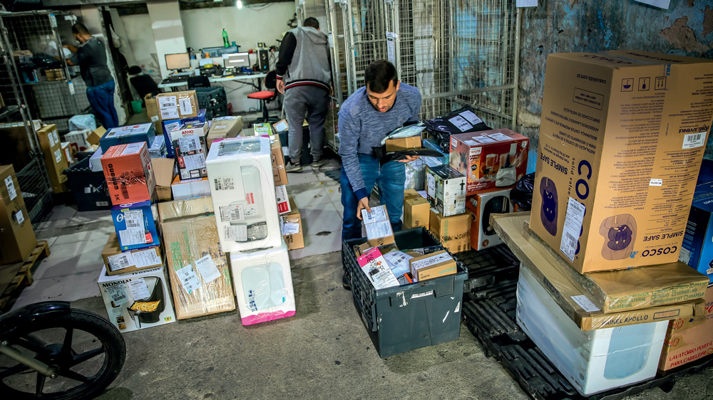 Trabalhadores em centro de distribuição repleto de caixas e pacotes