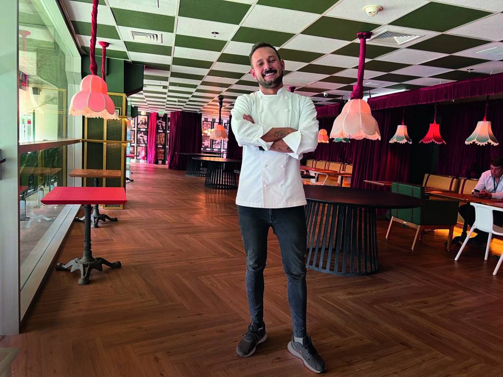 Chef Giovanni Renê posa em frente ao salão do La Coppa. Ao fundo, o salão e as mesas do restaurante.