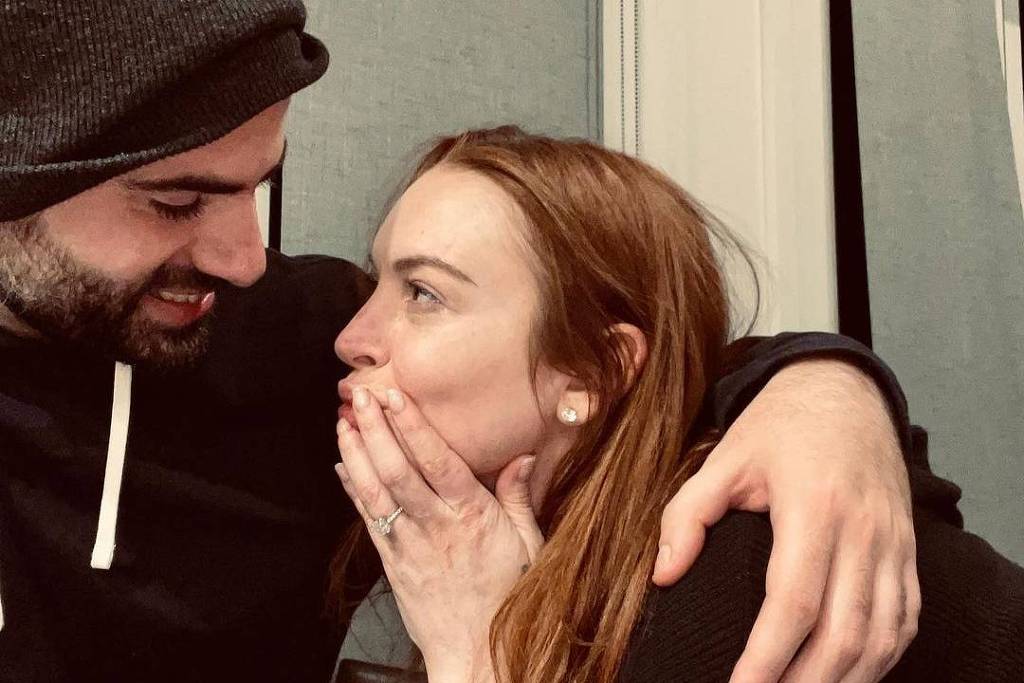 Foto exibe Lindsay com uma mão na boca ao lado do marido.