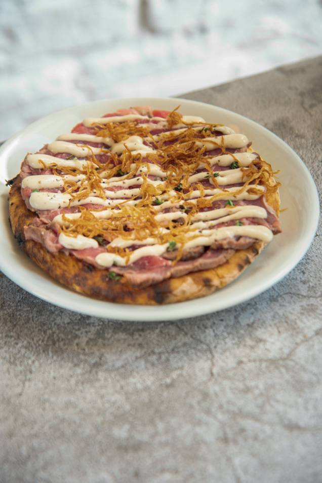 Ribeye tonatto: lâminas do corte, maionese de leite, molho de atum, aliche, alcaparras e crisps de cebola sobre disco de massa de pizza